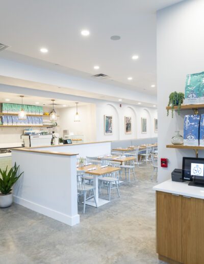The interior of a coffee shop with white walls and plants.